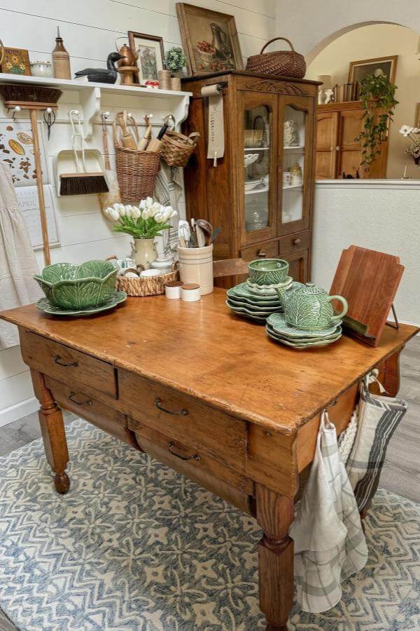 Sage green cabbage leaf ceramic dishes from @mamahensteph. Vintage-style dinnerware displayed on rustic wooden kitchen island.