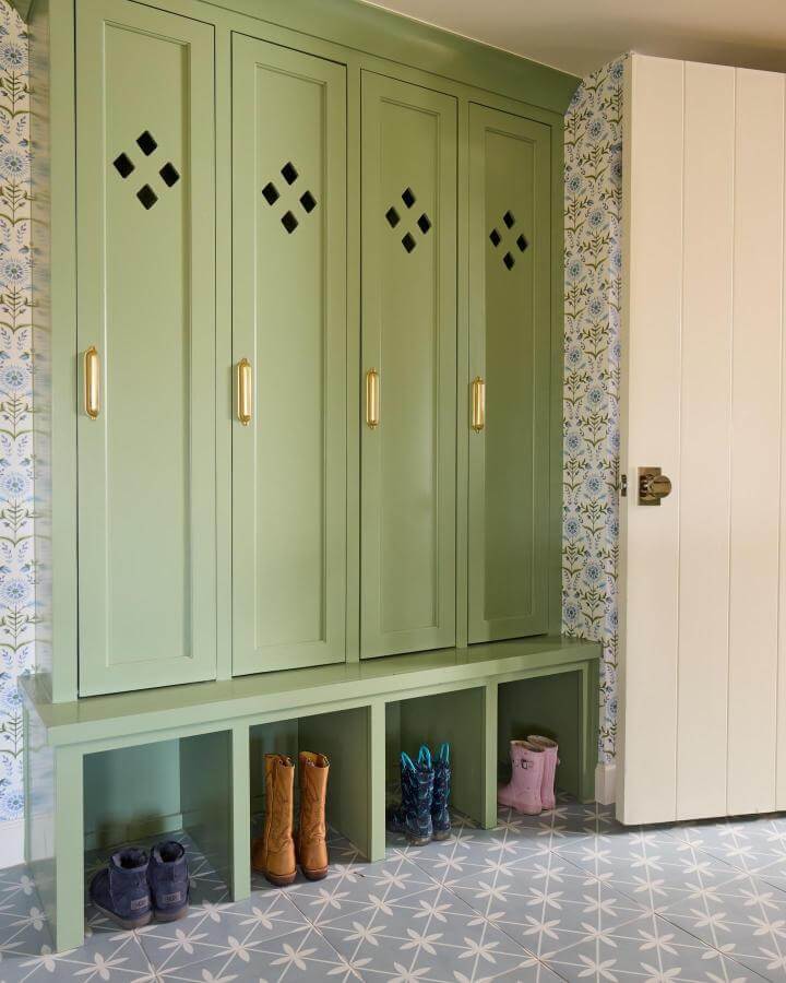 Sage green painted lockers and bench from @kaceygilpin with brass handles and floral wallpaper in mudroom entry space.
