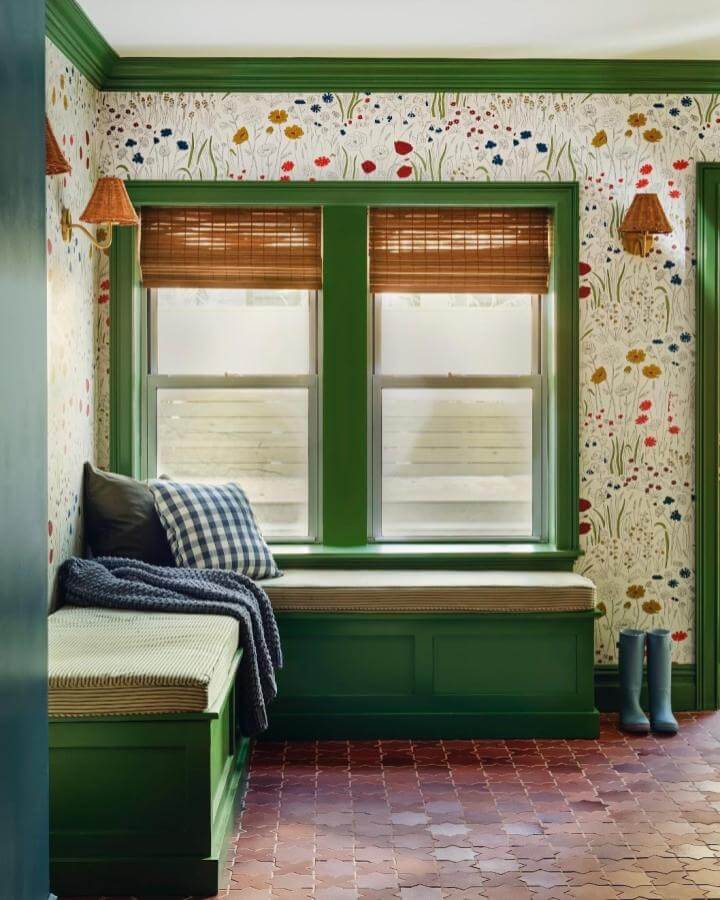 Green built-in bench nook with floral wallpaper and bamboo shades from @glamstudio_bk. Cozy and earthy mudroom seating area.