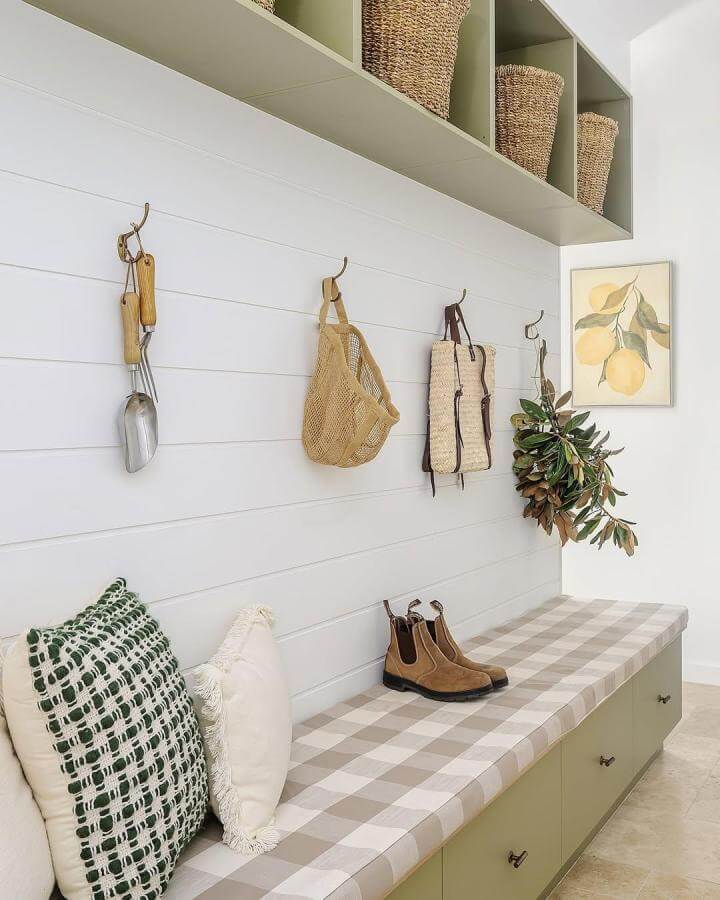 Soft sage green mudroom with built-in bench, brass hooks, and woven baskets from @coastpark.creative. Cozy, organized entryway design.