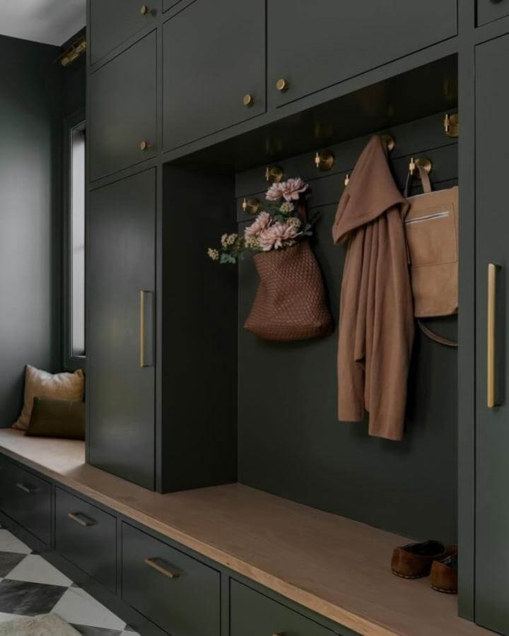 Dark green built-in mudroom storage with brass hooks and wooden bench seat by @hayeshouseco. Cozy organized entryway space.