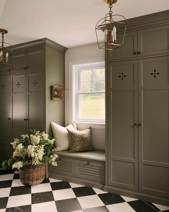 Olive green built-in mudroom cabinetry and cozy bench seat from @sylvieli with contrasting black and white checkerboard floor in green mudroom ideas.