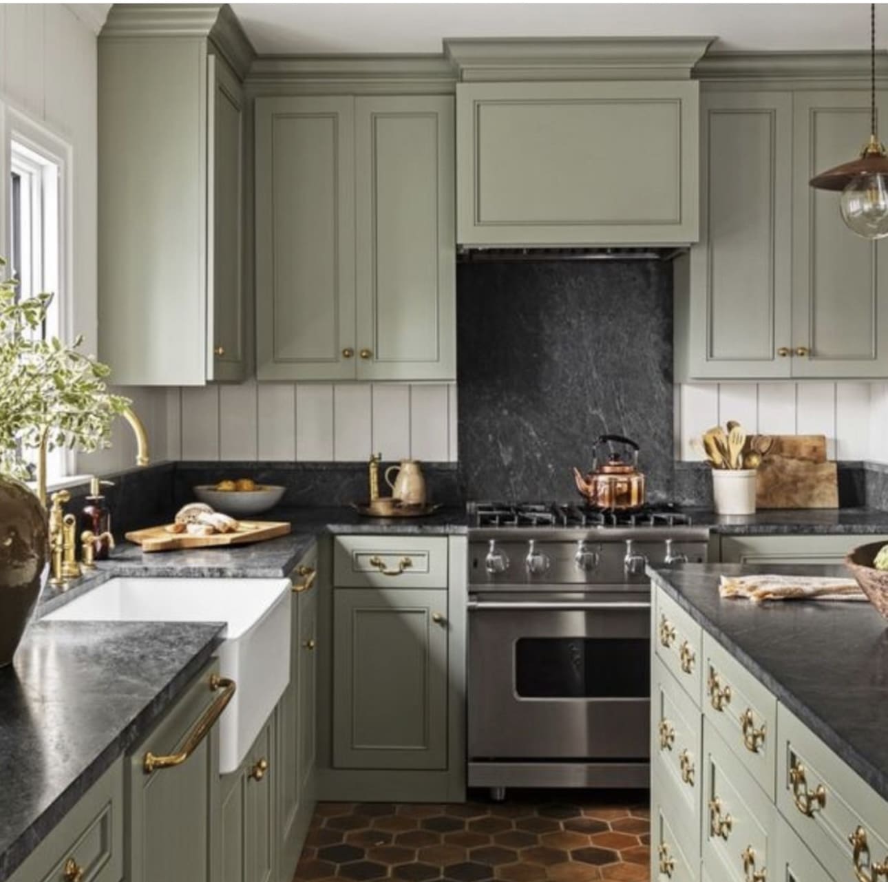 Sage green cabinets frame a dramatic dark stone backsplash