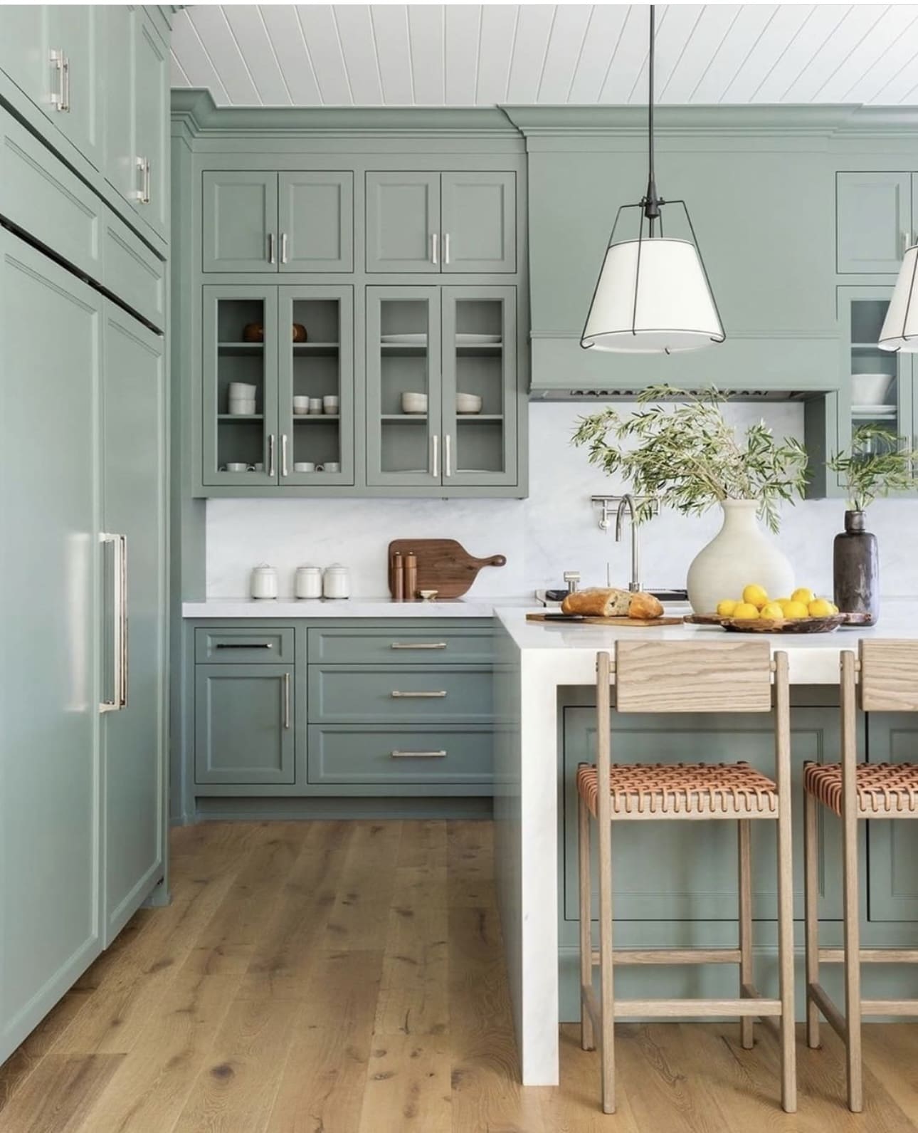 Sage green glass-front cabinets display curated dishware