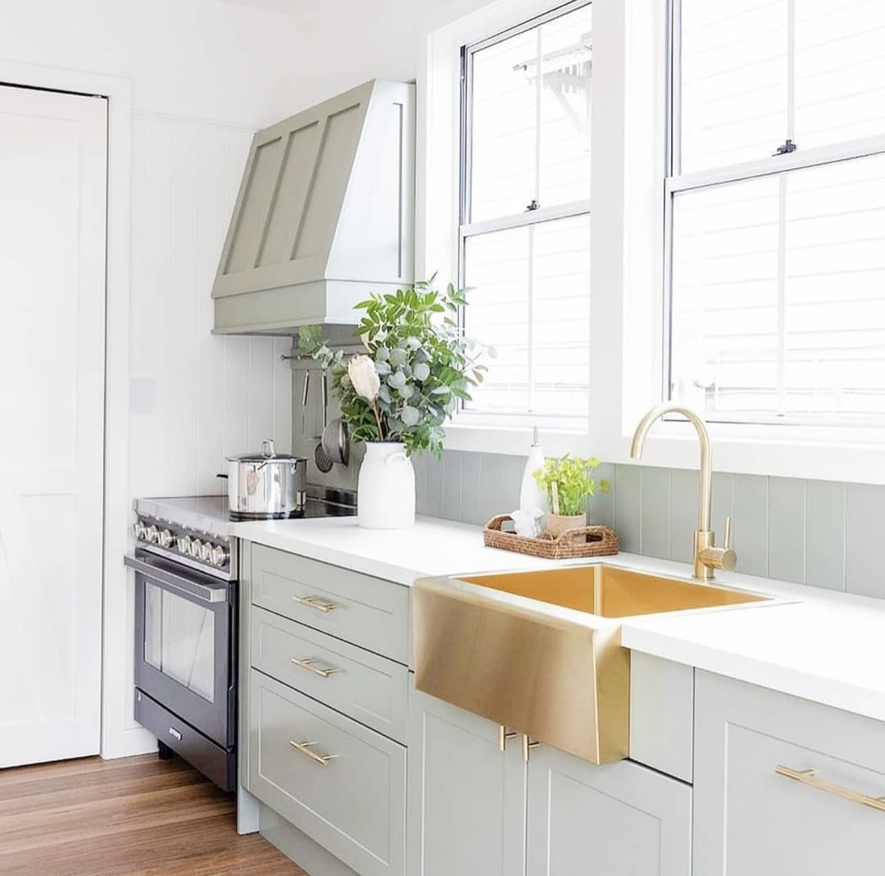 Sage green cabinets frame a metallic brass farmhouse sink