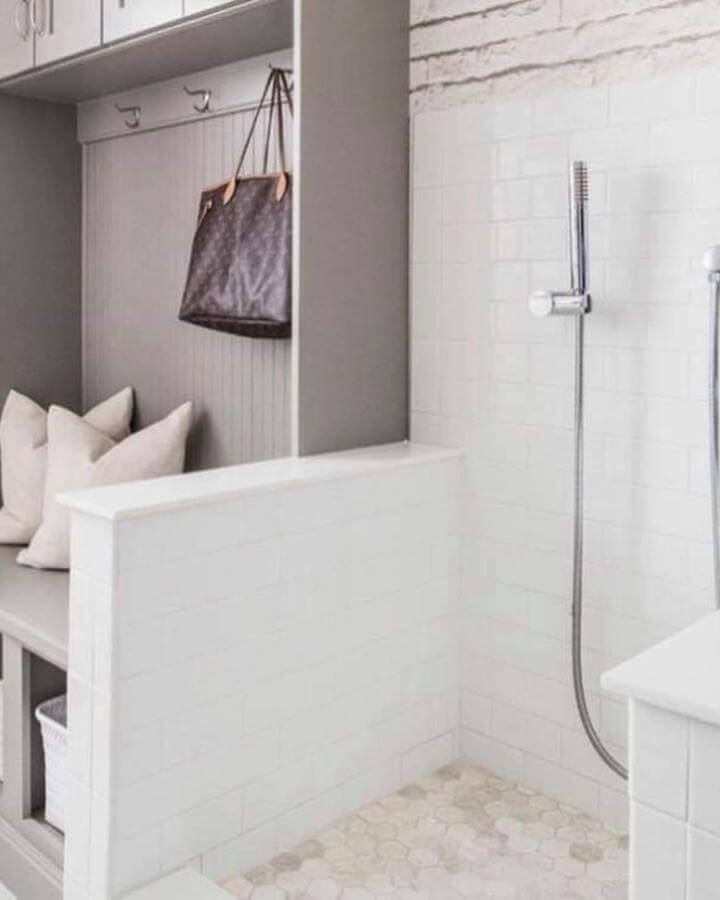 White tiled pet wash area with half wall and gray beadboard bench from @tinamarieinteriordesign. Functional and stylish dog cleaning space.
