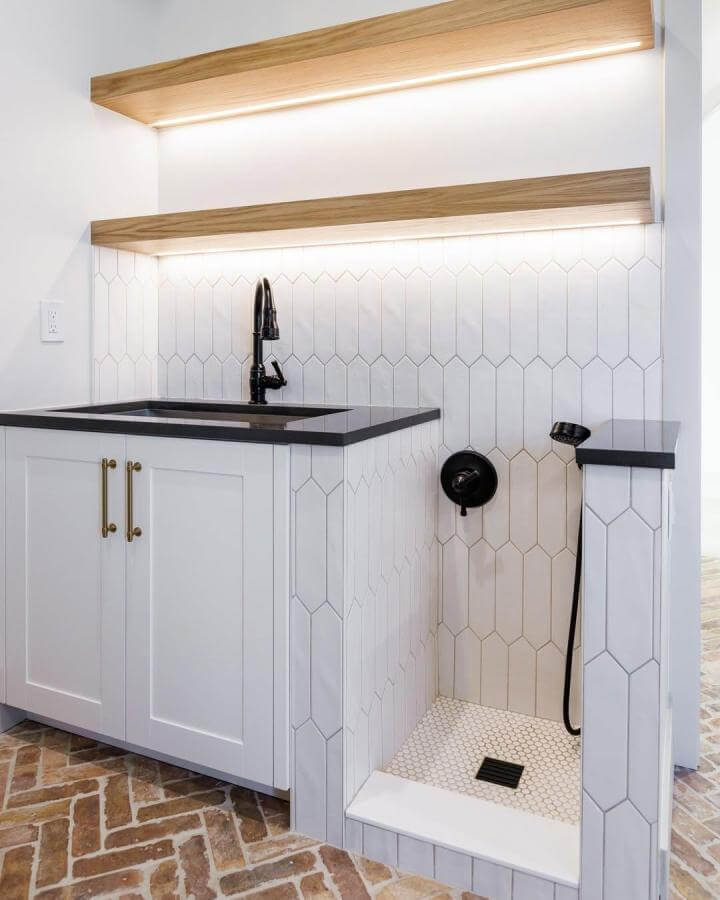 White tile mudroom dog wash with black faucet and sprayer, wood shelves and black countertops by @mindygeraetsphotography. Bright, modern, functional pet wash area.