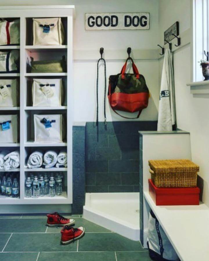 Slate tile mudroom dog wash area with white shelving, canvas bins, and playful
