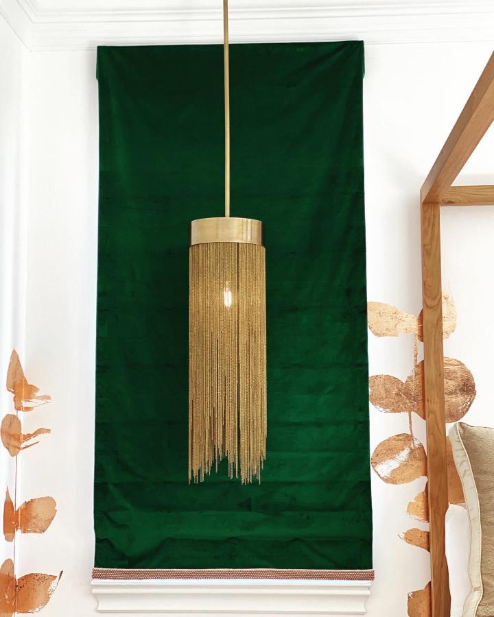 Deep emerald fabric wall panel from @dianalombardinteriors. Golden fringe pendant light creates luxurious bedroom focal point.