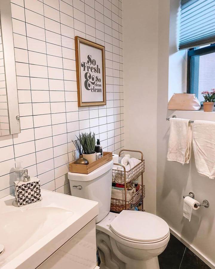 White tiled bathroom wall with black grout and slim wire basket storage from @mystamfordhome brightens and organizes a compact washroom space.