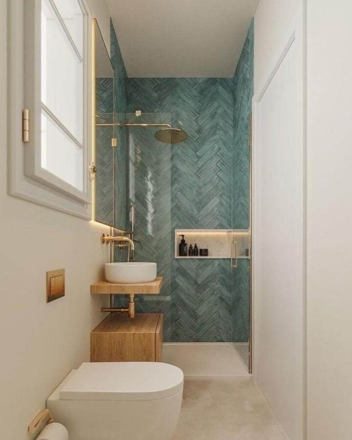 Teal herringbone tile bathroom with wooden vanity and gold fixtures from @tamburic in a compact space.